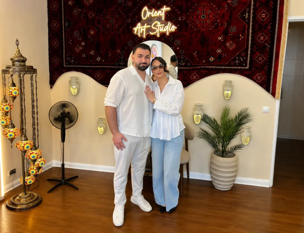 Ferhat und Dilara Taşkın vor dem Orient Art Studio in Berlin mit orientalischer Einrichtung und leuchtendem Studioschild.